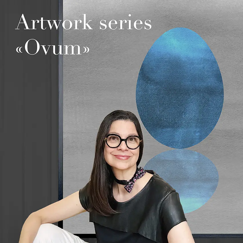 Picture of a woman with dark hair and dark eyeglasses. She is sitting in front of a big framed picture, representing a blue egg shaped form with a light blue reflection on the ground. The background is grey. There is a white text in the upper left corner.